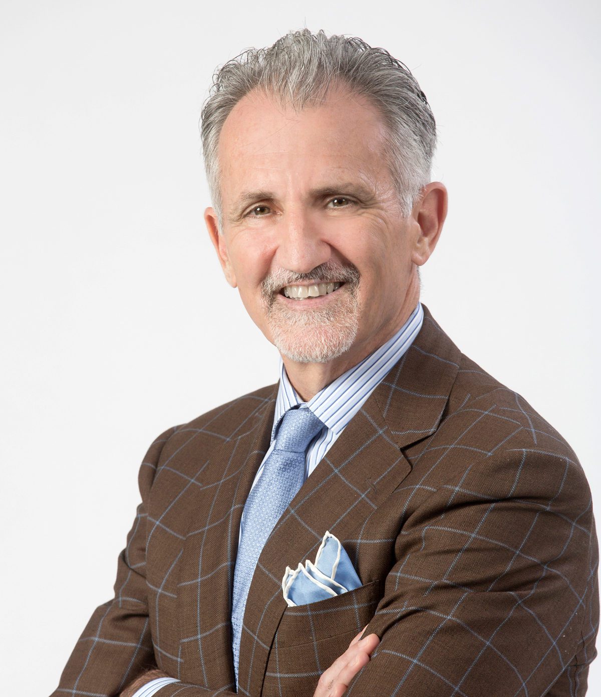Professor George Bisharat smiles while wearing a brown checkered suit with a light blue tie and pocket square, arms crossed against a plain background.