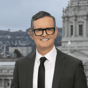 A headshot phot of Morris Ratner in a suit and tie with San Francisco City Hall dome in the background.