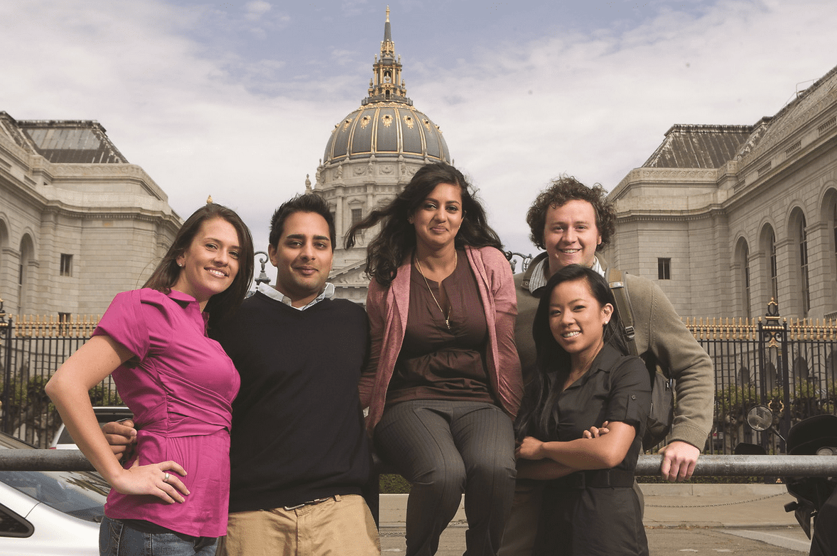 UC Law SF community members sitting outside smiling and looking at the camera with SF city hall domed building in the backdrop