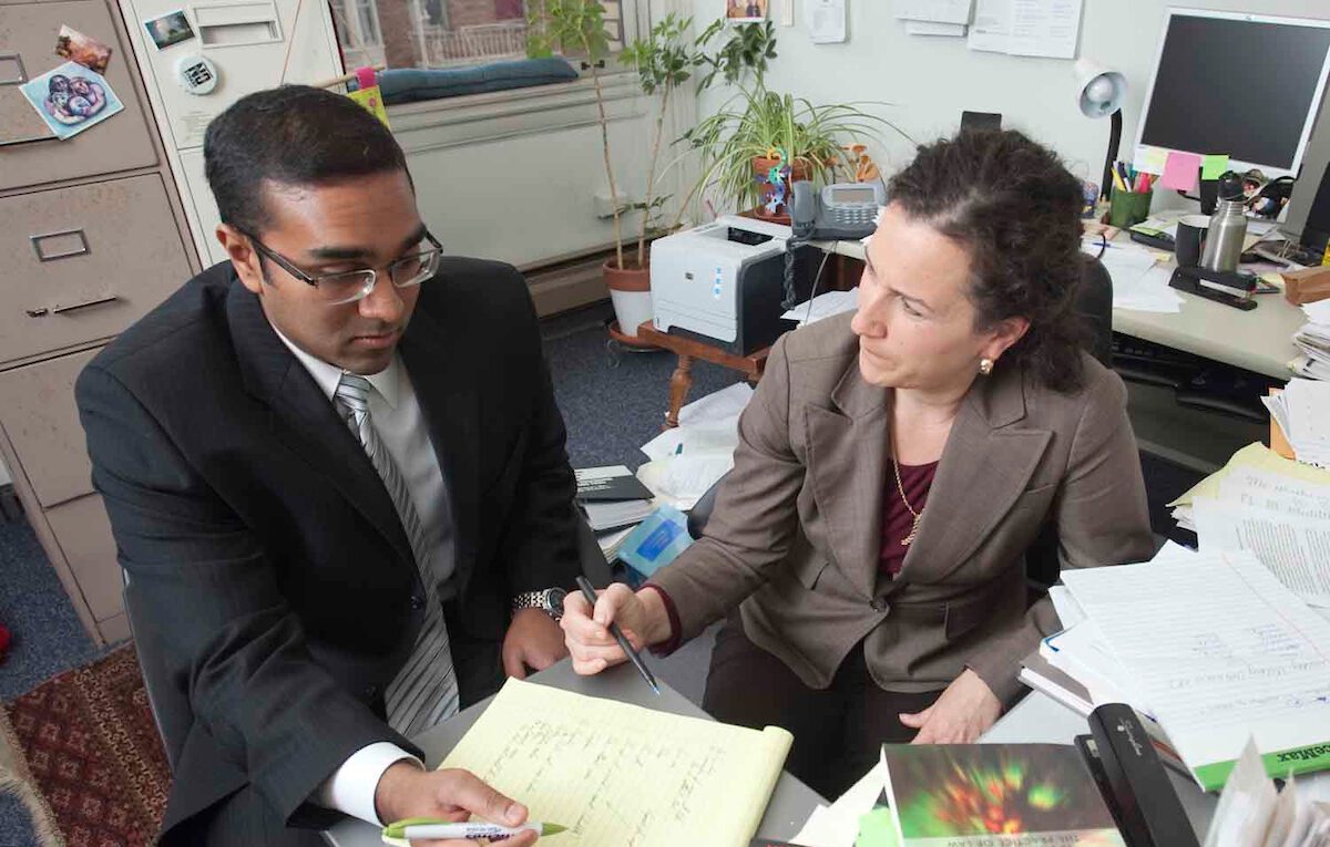 A faculty member with student, sitting at a desk, going over notes on a yellow notepad