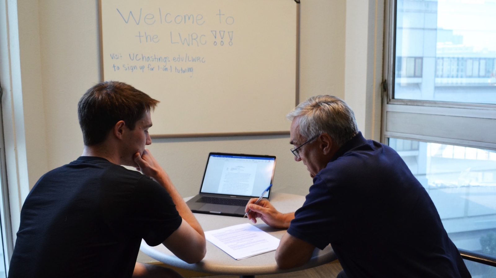 A teacher and student sitting in a LWRC conference space reviewing a paper.