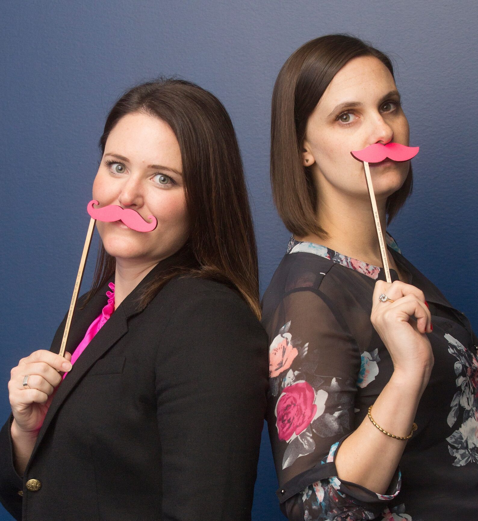 Two women, back-to-back, holding up pink Lyft moustaches