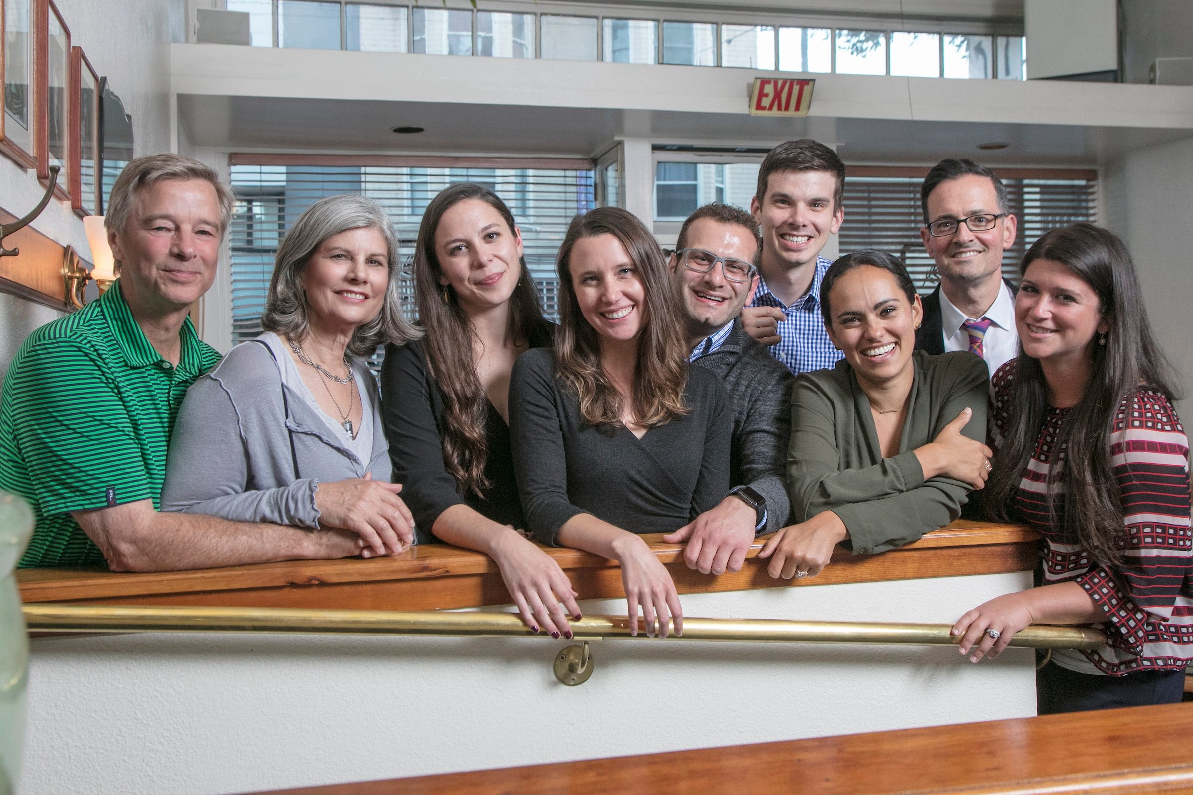 Scholarship recipients gather together indoors, leaning over a stair railing. They are smiling and looking at the camera