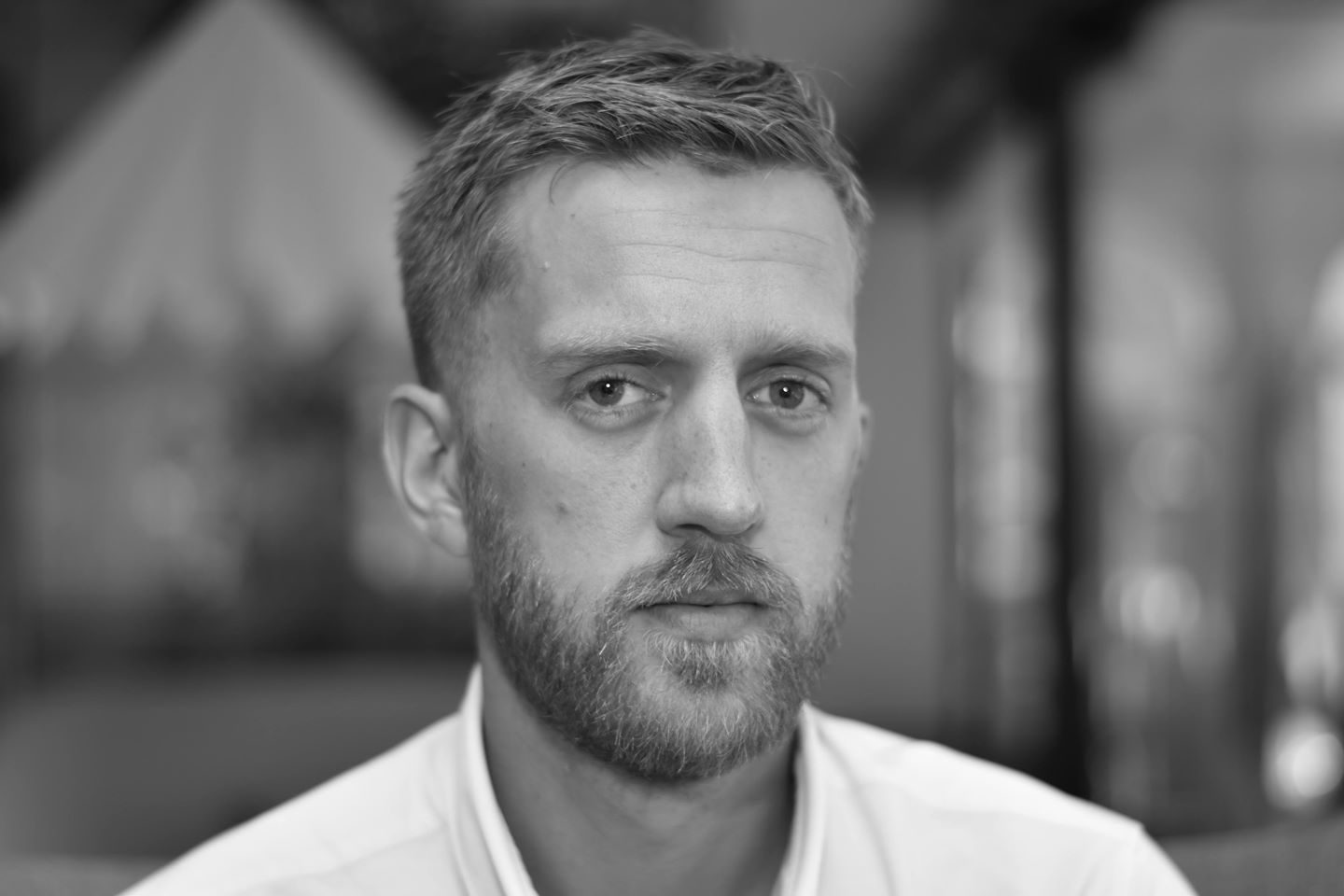 Black and white photo of a man looking at the camera wearing a white top