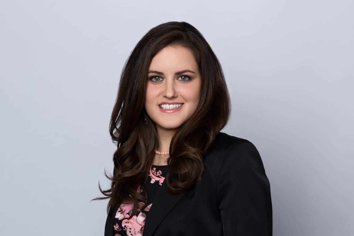 Woman smiling and looking at the camera, wearing a flowery top and black suit jacket