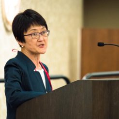 Carol Izumi speaks at podium