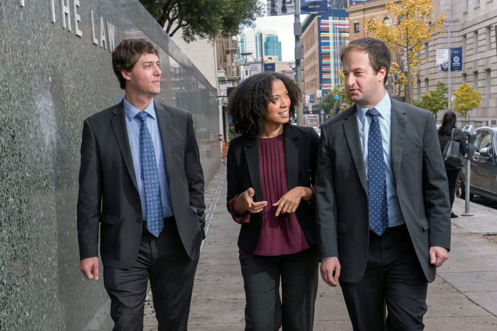 Professors walking together on a city sidewalk, discussing animatedly in business attire, with a modern urban backdrop visible.