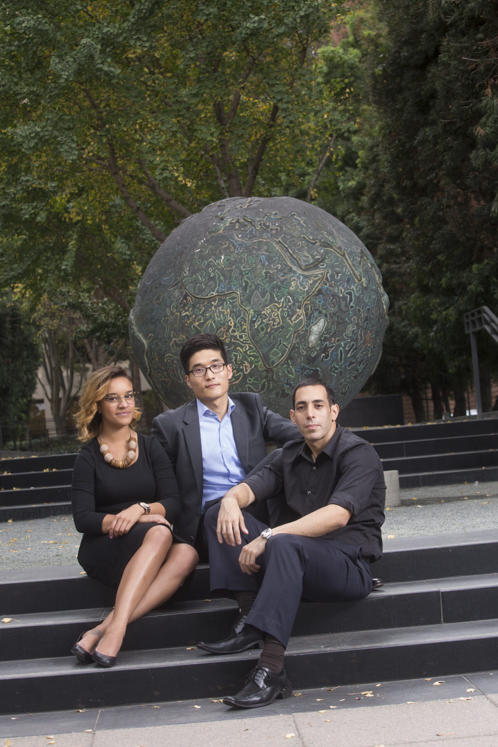 3 Hastings community members sitting on steps by statue