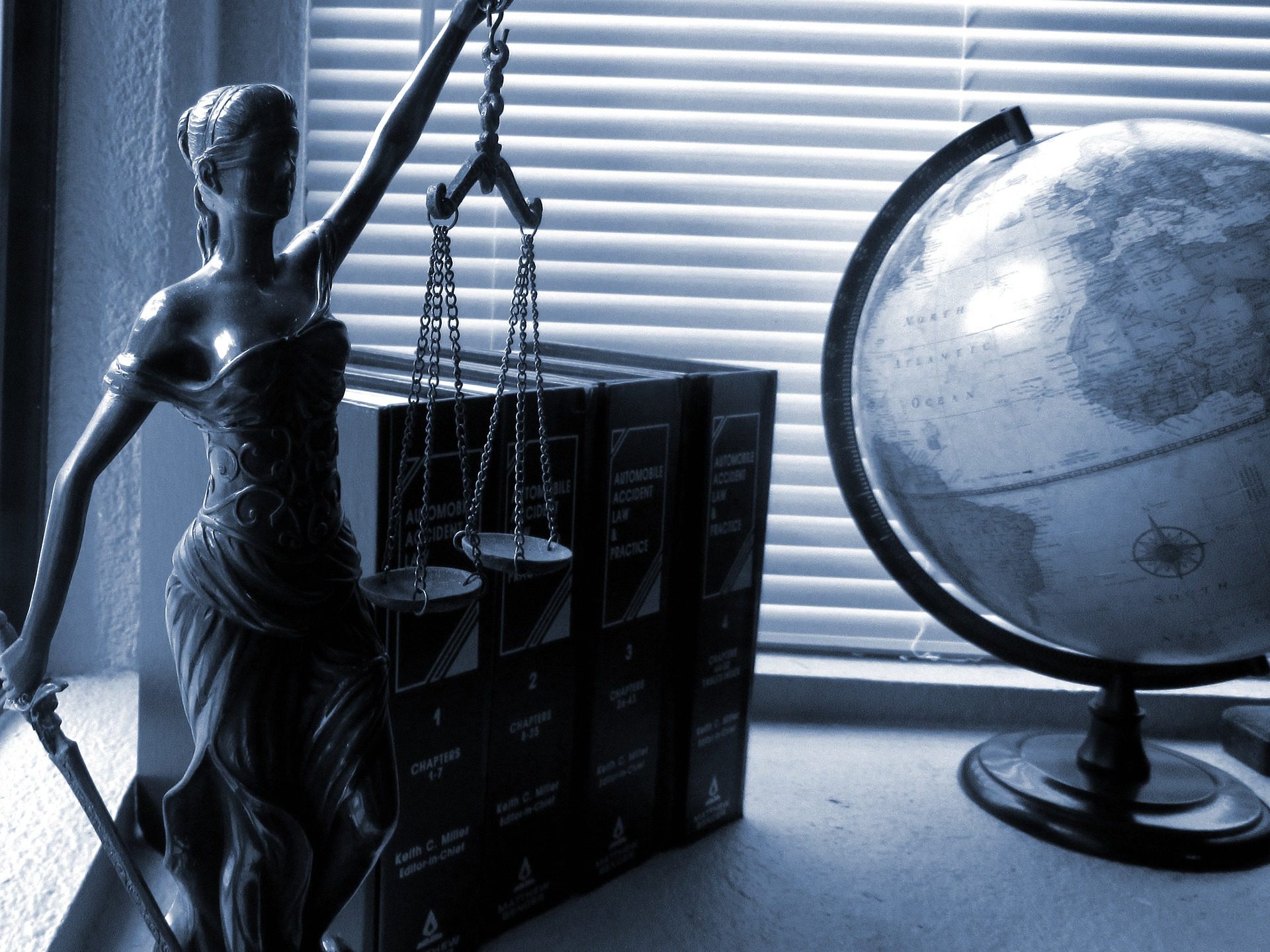 statue of lady justice holding scales with textbooks and a globe in the background