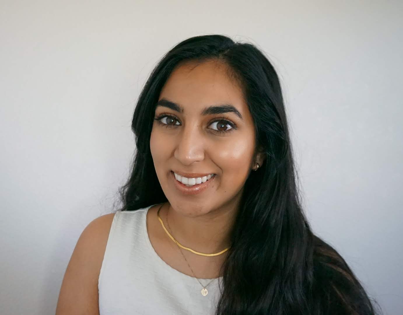 Woman smiling at the camera, wearing a white top and gold necklace. White backdrop