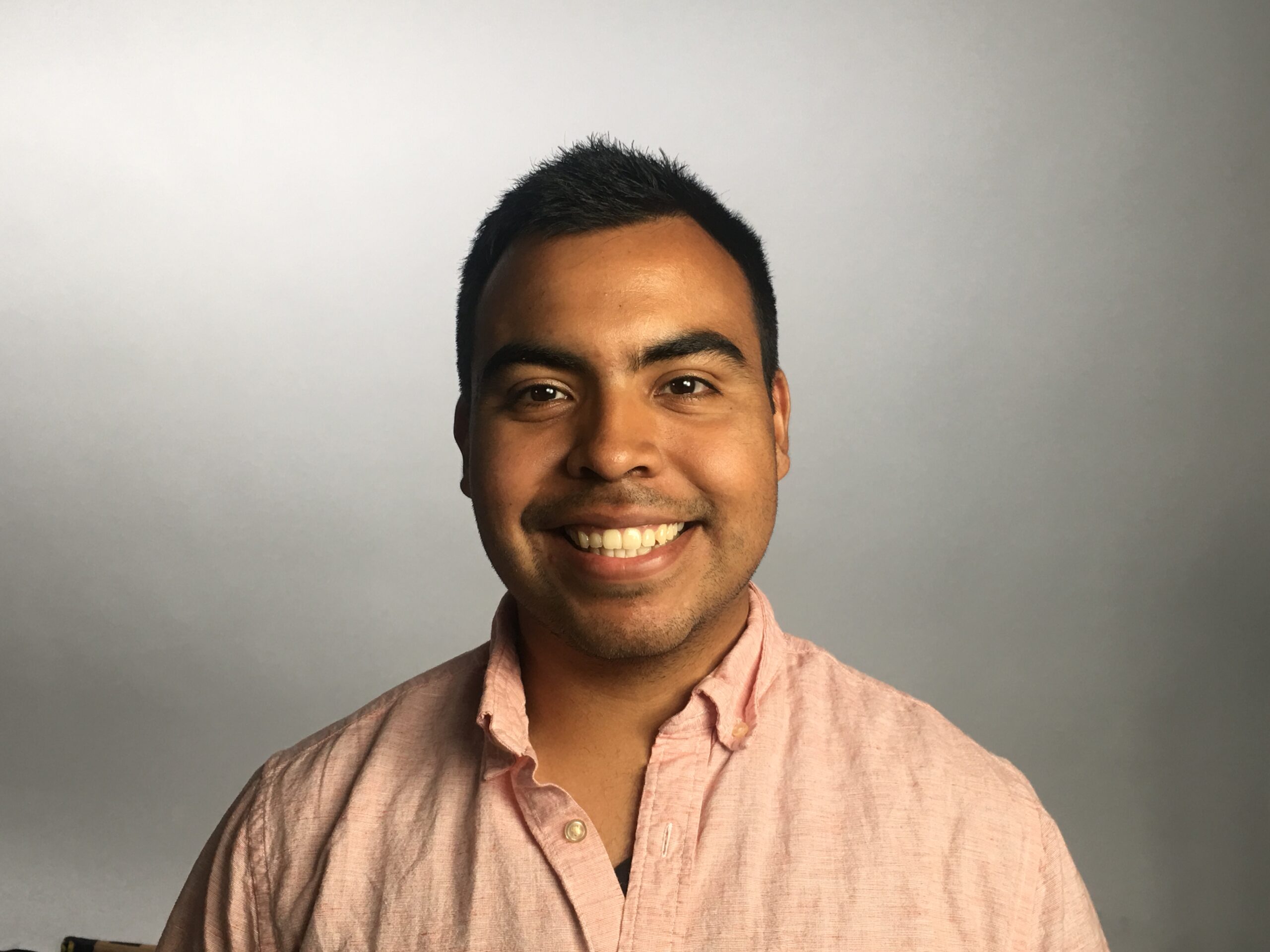 Jacob Barrera smiles at the camera, wearing a light pink button-up shirt, against a neutral gradient background.