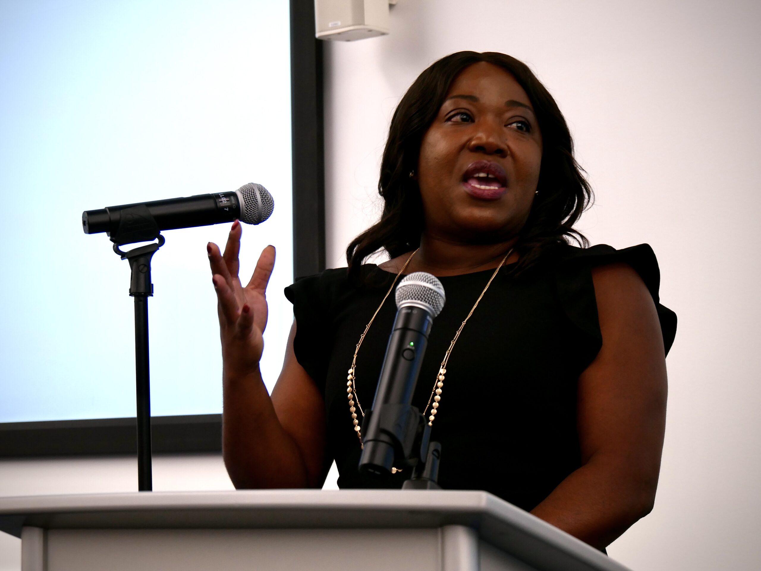 A woman stands at a podium speaking into a microphone during a convocation ceremony for incoming JD students at UC Law SF.