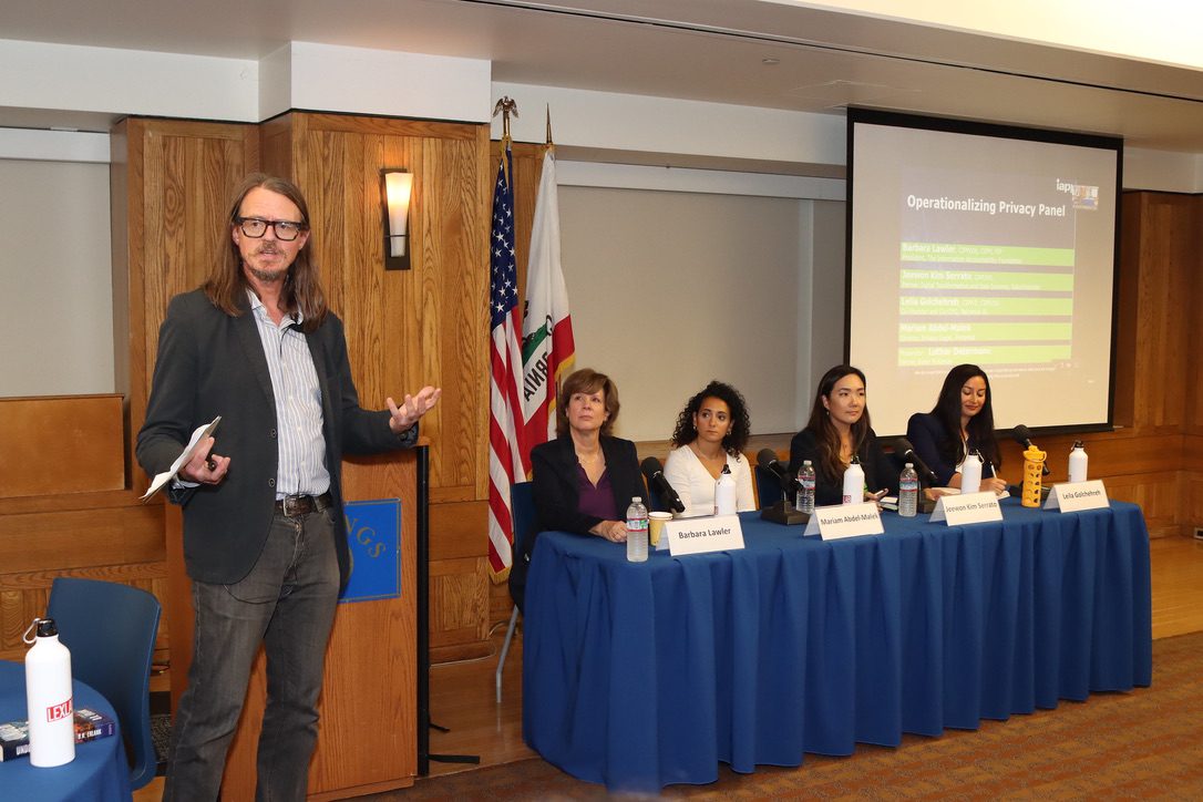 man with long hair and glasses stands near table of professional women