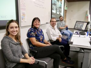 Upper-division law students and a professor sit in a classroom during a social justice event, with a presentation displayed on screens behind them.
