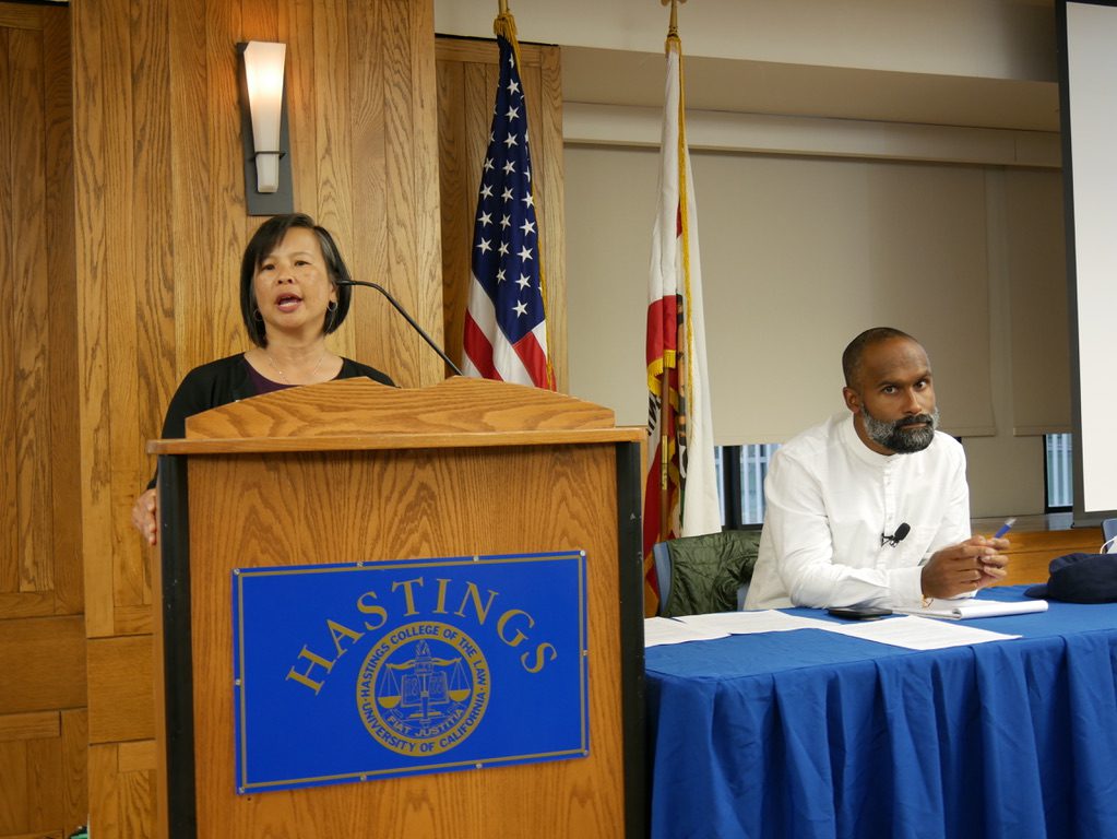 ACLU attorney Grace Hum speaks at UC Law SF, addressing free speech, academic freedom, and racial justice, with flags in the background.