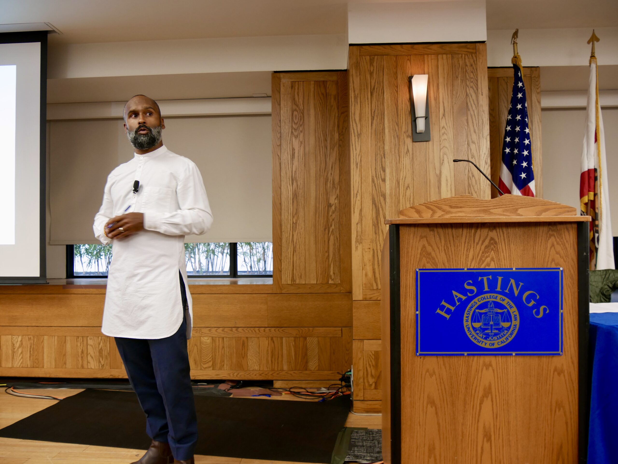 ACLU attorney Emerson Sykes speaks at UC Law SF about free speech, academic freedom, and racial justice, standing in front of a podium and flags.