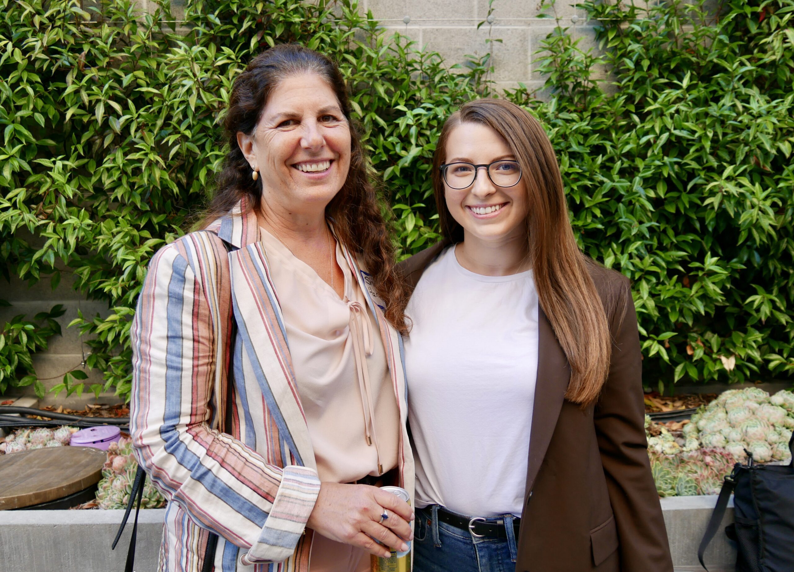 two women smile in front of foliage