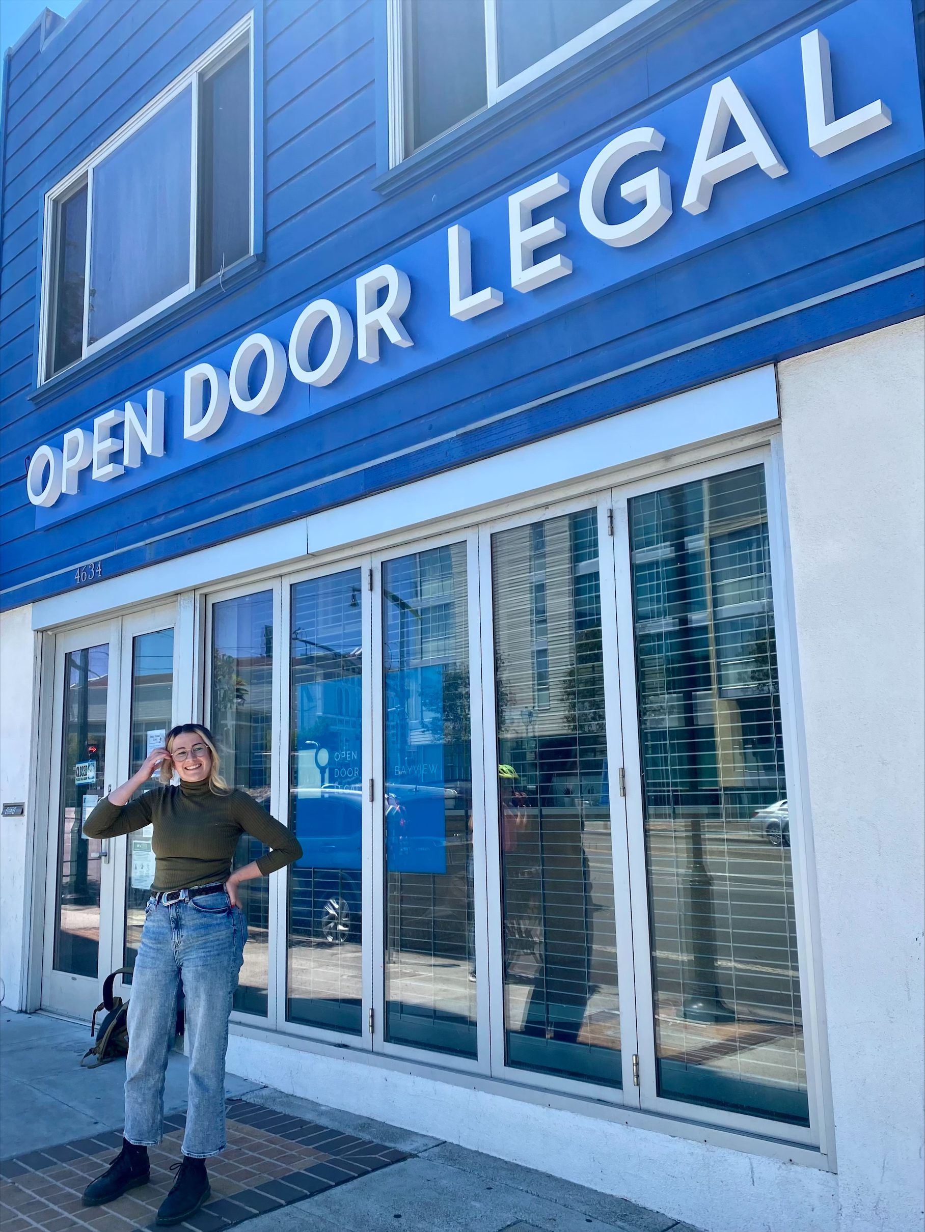 UC Law SF student Rachel Pyle stands outside Open Door Legal, a nonprofit offering legal assistance, smiling and posing with her hand on her hip.