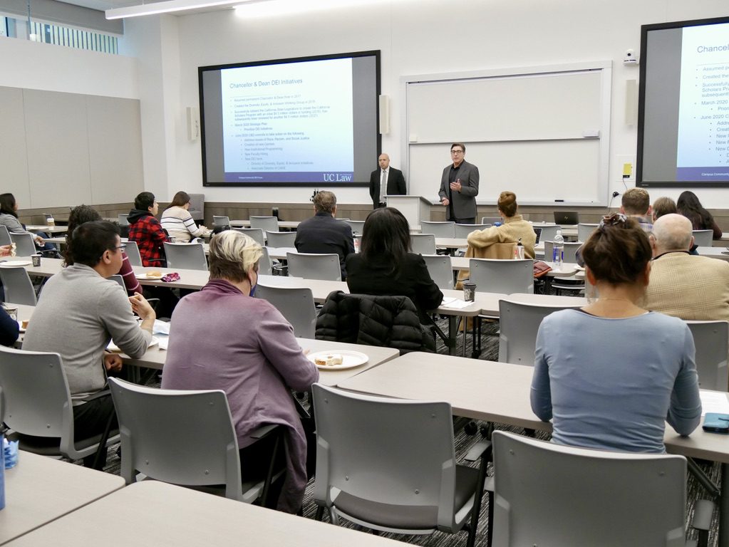 A forum held at UC Law SF with attendees discussing diversity, equity, and inclusion initiatives while two speakers present information on a screen.