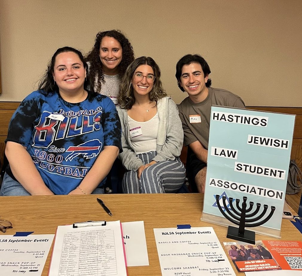 Members of the Jewish Law Students Association sit together at a table during a Fall 2022 student organization fair. A sign for their group is displayed next to them.