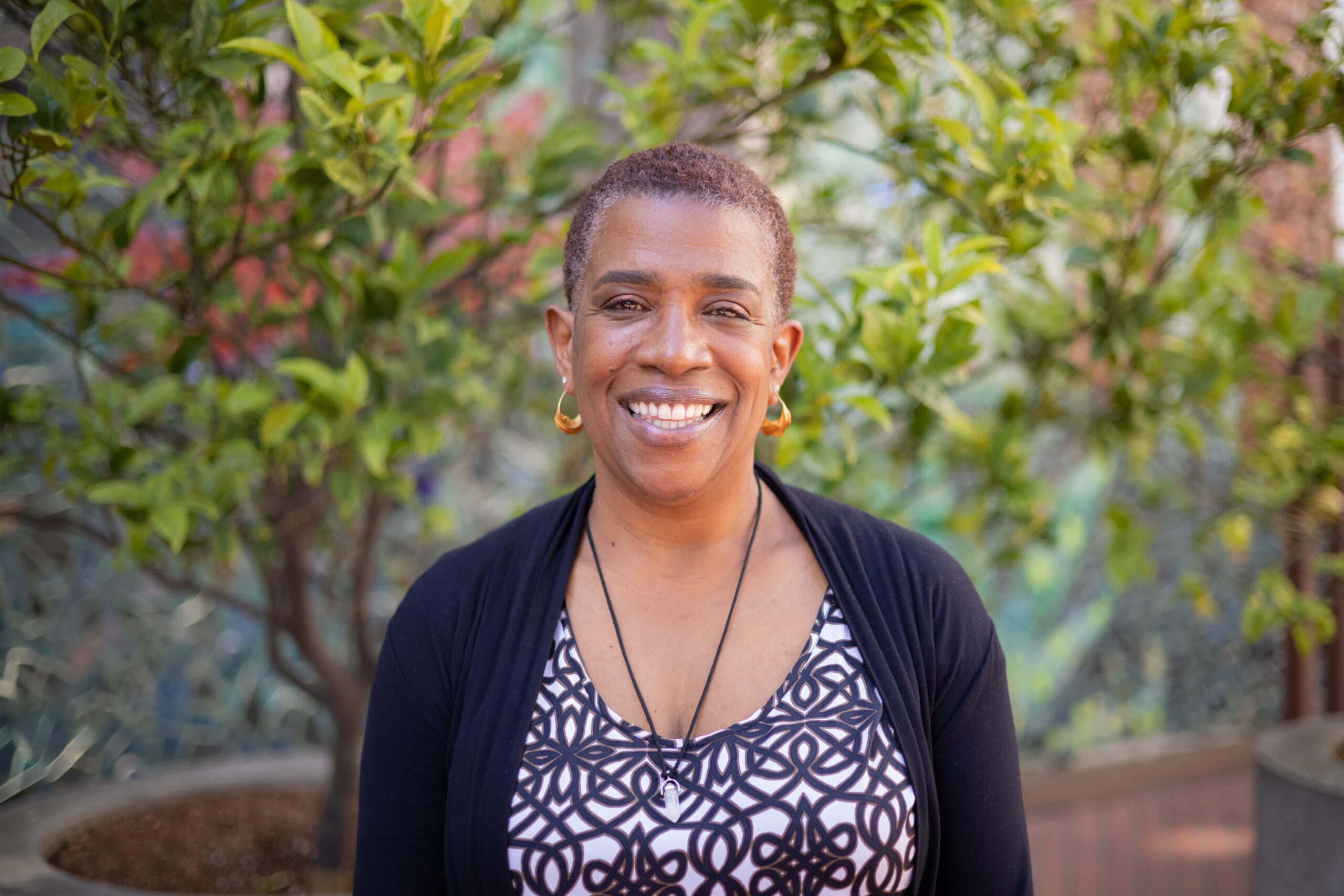 Kelly Dearman smiles in front of greenery, wearing a patterned top and a cardigan. She is the executive director of the San Francisco Department of Disability and Aging Services.