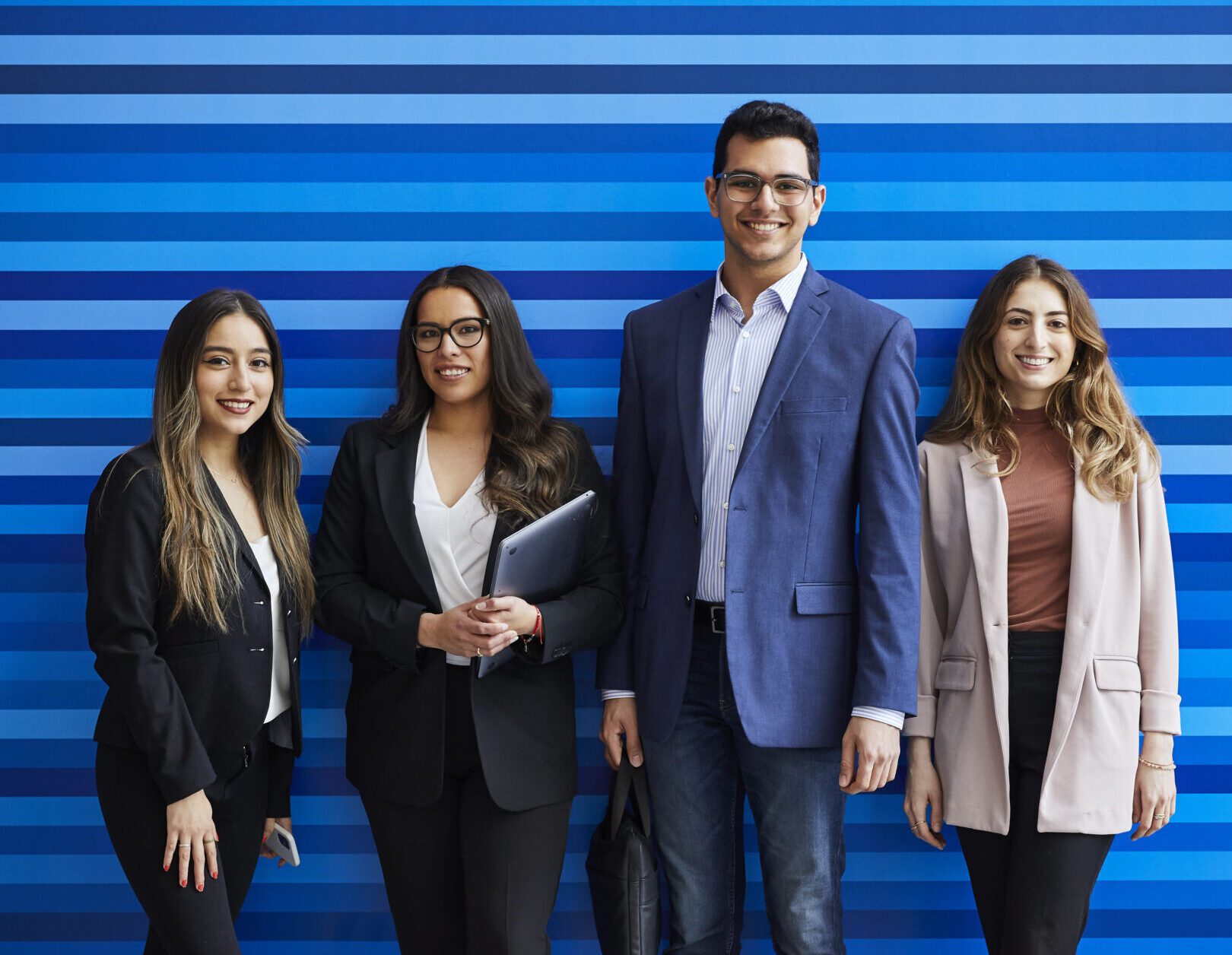 students smiling at camera and standing in front of a blue striped background