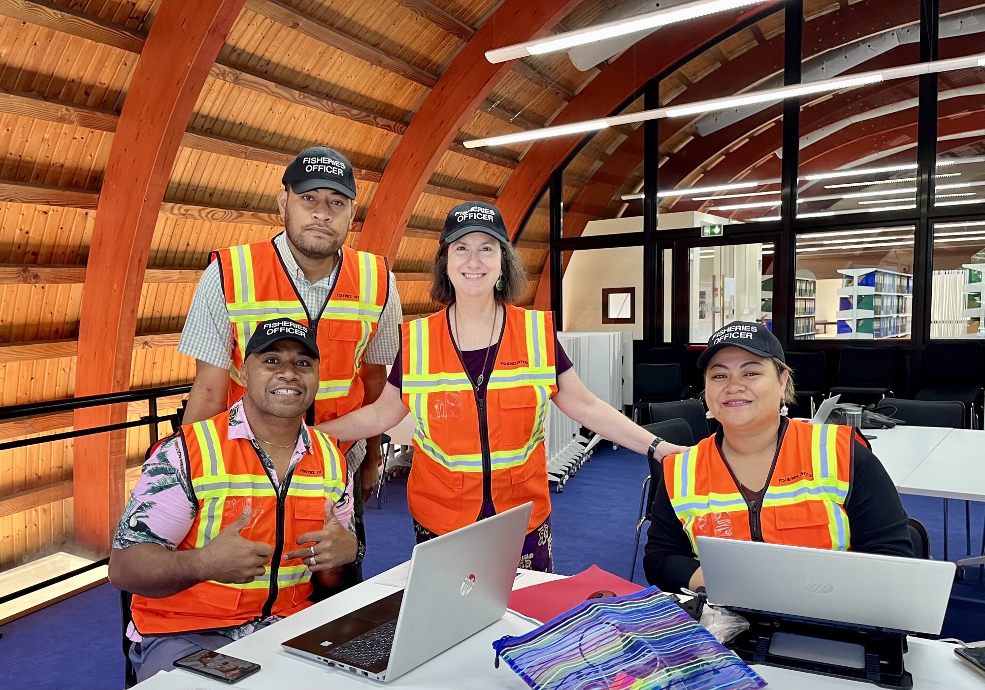 Jessica Vapnek and three delegates from Pacific countries, all wearing bright safety vests and hats marked "Fisheries Officer," pose for a photo during a workshop.
