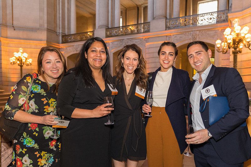 Alumni gathered at San Francisco City Hall for an elegant party, enjoying passed champagne and gourmet food in a grand setting.