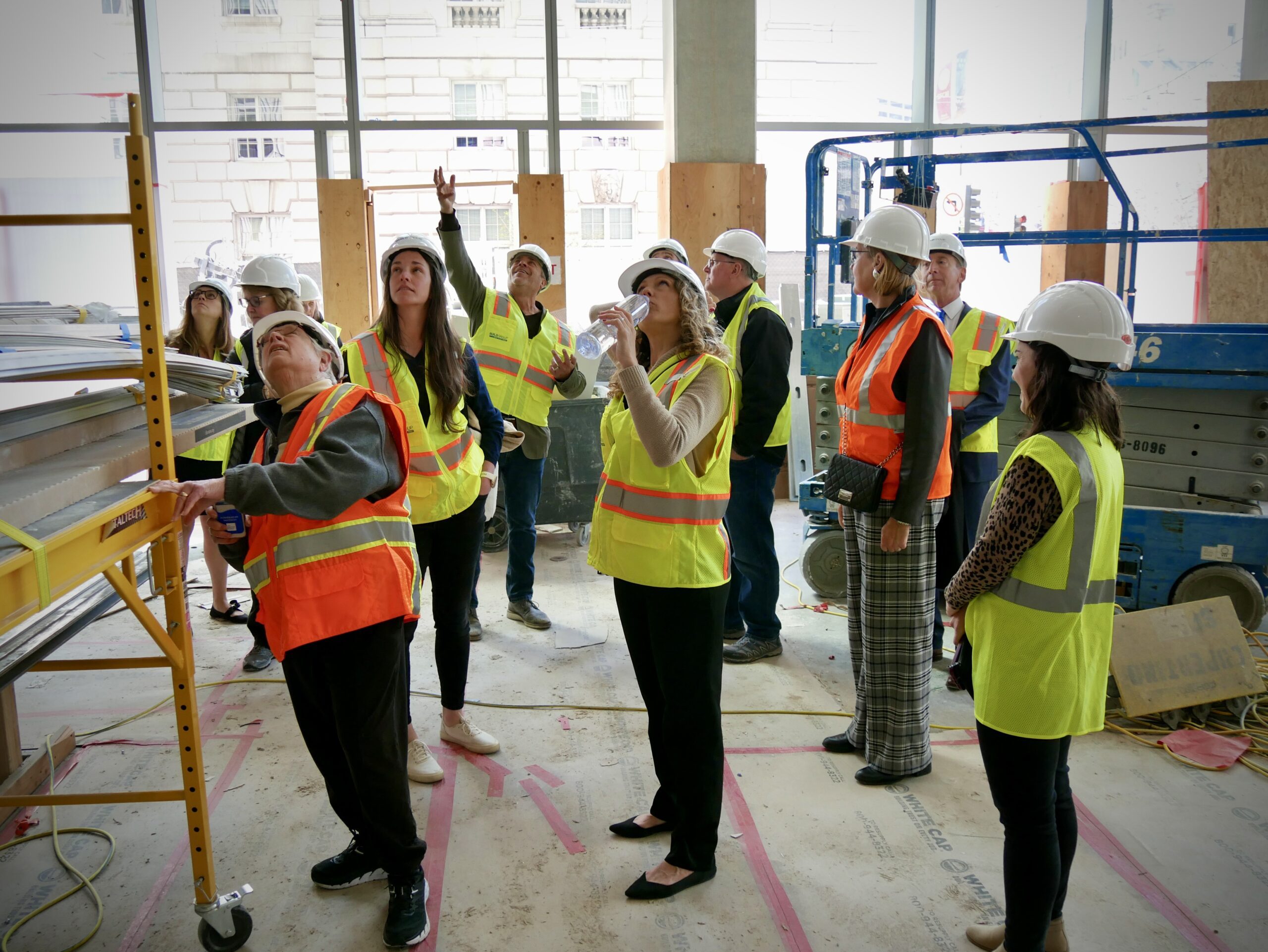 Visitors in hard hats and safety vests tour a construction site with exposed beams and materials, observing the ongoing building project.