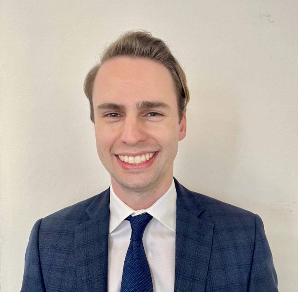 Andrew Hudlow smiles while wearing a suit and tie against a plain background, representing his role as treasurer and soon-to-be president of the UC Law San Francisco chapter of the Federalist Society.