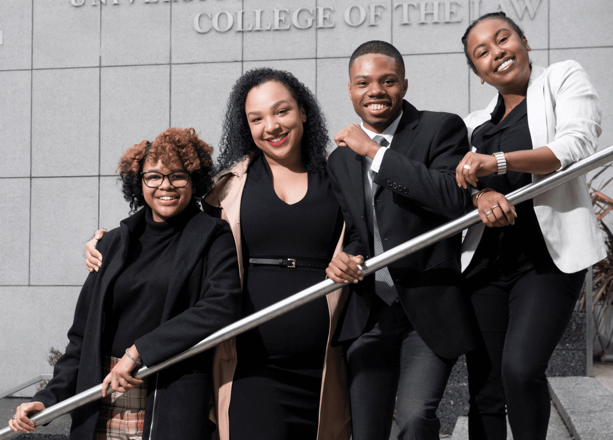 students smiling at the camera and leaning on a staircase railing