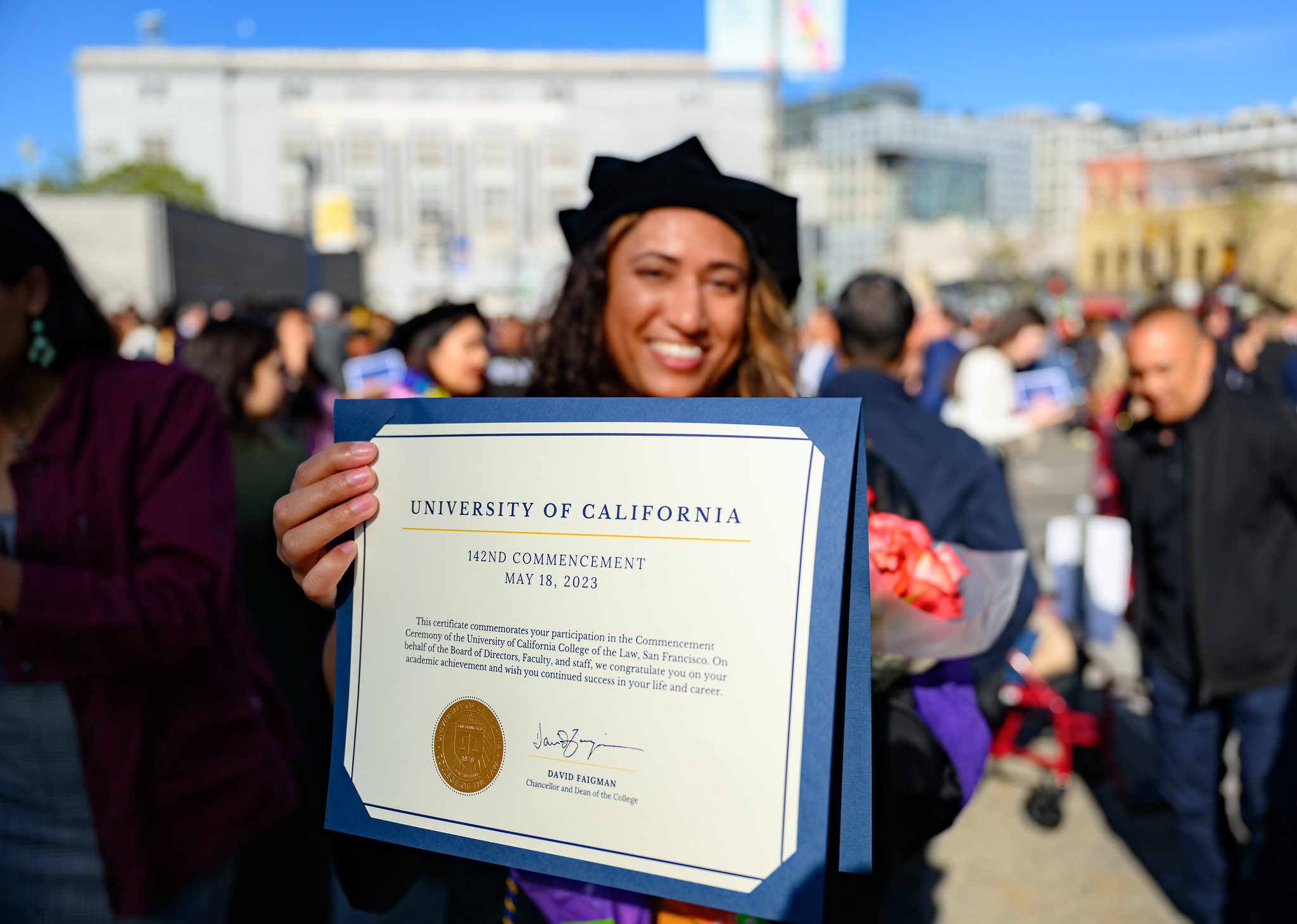 student smiling at the camera and holding their degree towards the camera