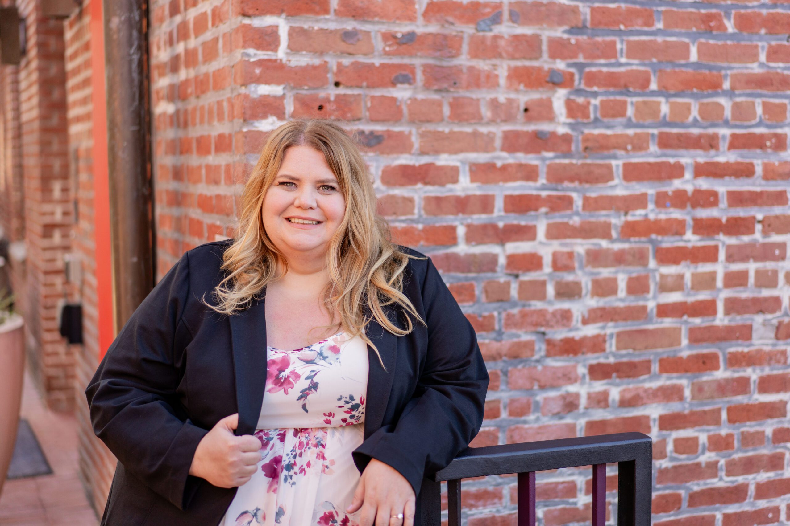 Woman smiling and looking straight at the camera. She is wearing a black suit jacket and floral top.