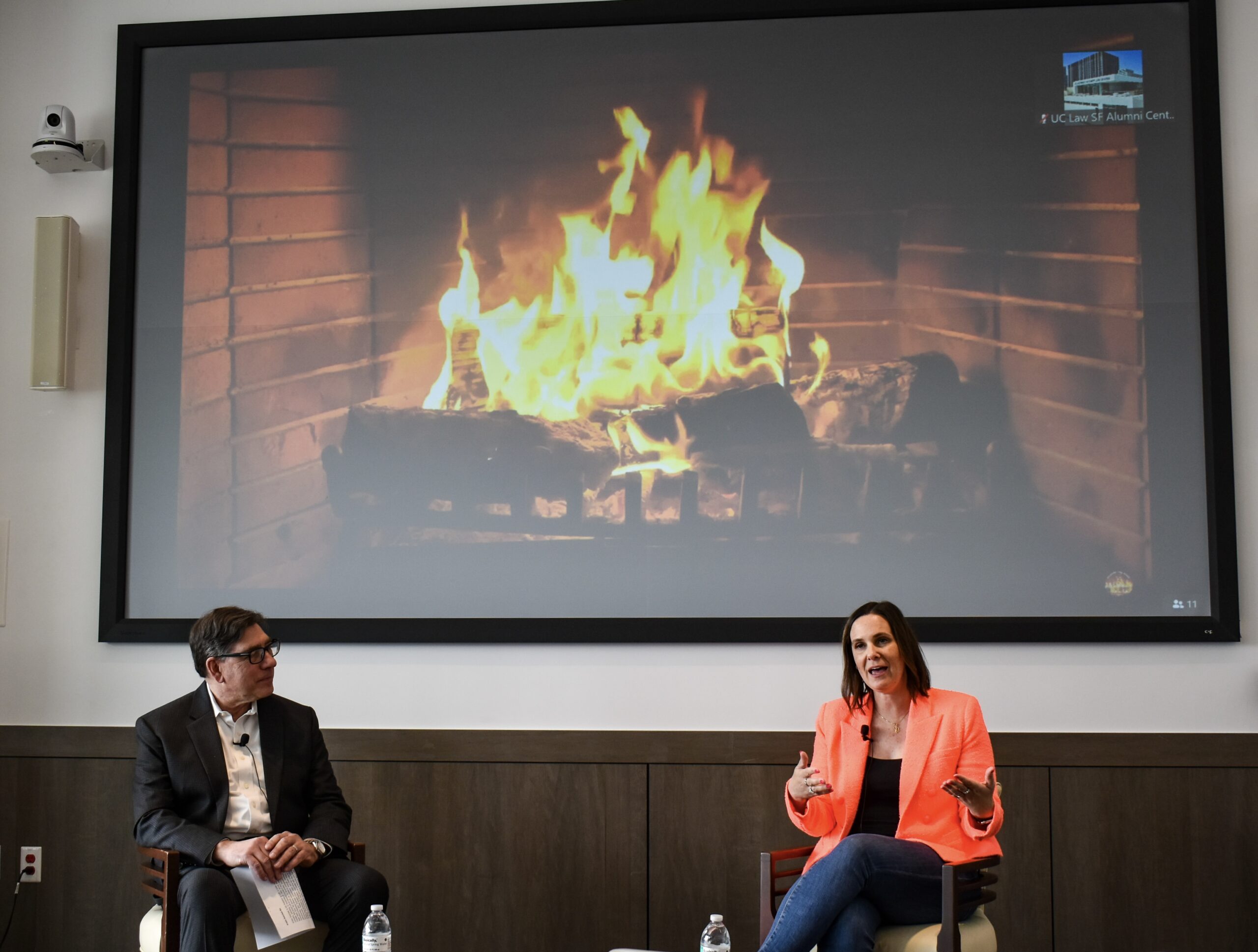 Lyft President Kristin Sverchek ’07 with Chancellor & Dean David Faigman. A projection of a burning fireplace is behind them.