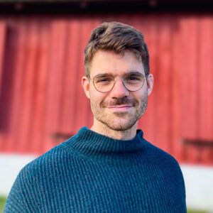 a headshot photo of Benjamin Barsky in a blue sweater with eyeglasses and a mustache.