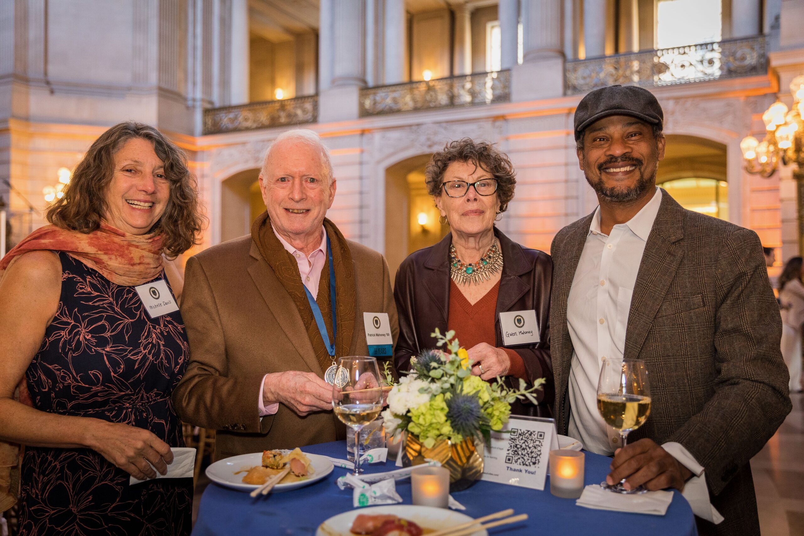 Four UC Law SF alumni standing behind a table inside San Francisco City Hall