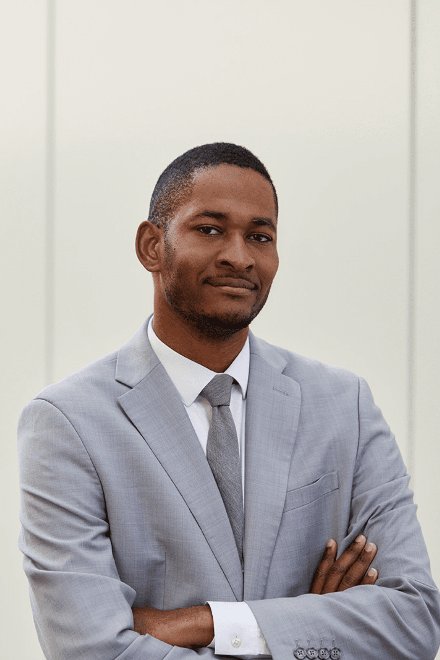 A student looks confidently into the camera with his arms crossed. He wears a gray suit.