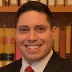 Image depicting J. Joel Alicea, an Associate Professor of Law, smiling in front of a bookshelf filled with law books.