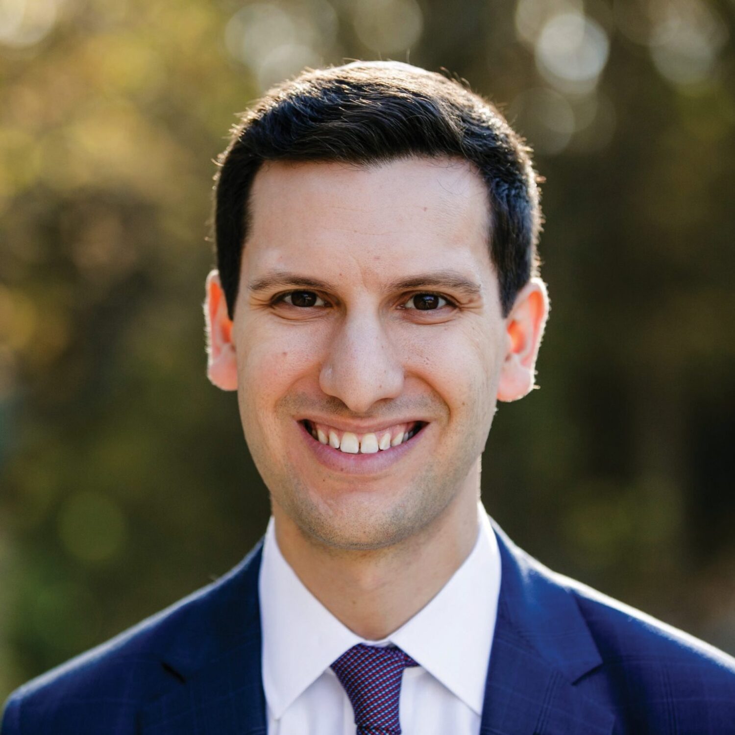 Smiling Jonathan Gould Professor of Law UC Berkeley Law in a suit with short dark hair, standing outdoors against a blurred background of trees.