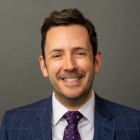 Smiling image of Charles Tyler Assistant Professor of Law, UC Irvine School of Law in a blue suit with a grey background.