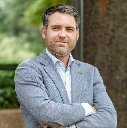 Smiling image of Daniel Walters Associate Professor of Law, Texas A&M School of Law with arms crossed and blurred nature background.