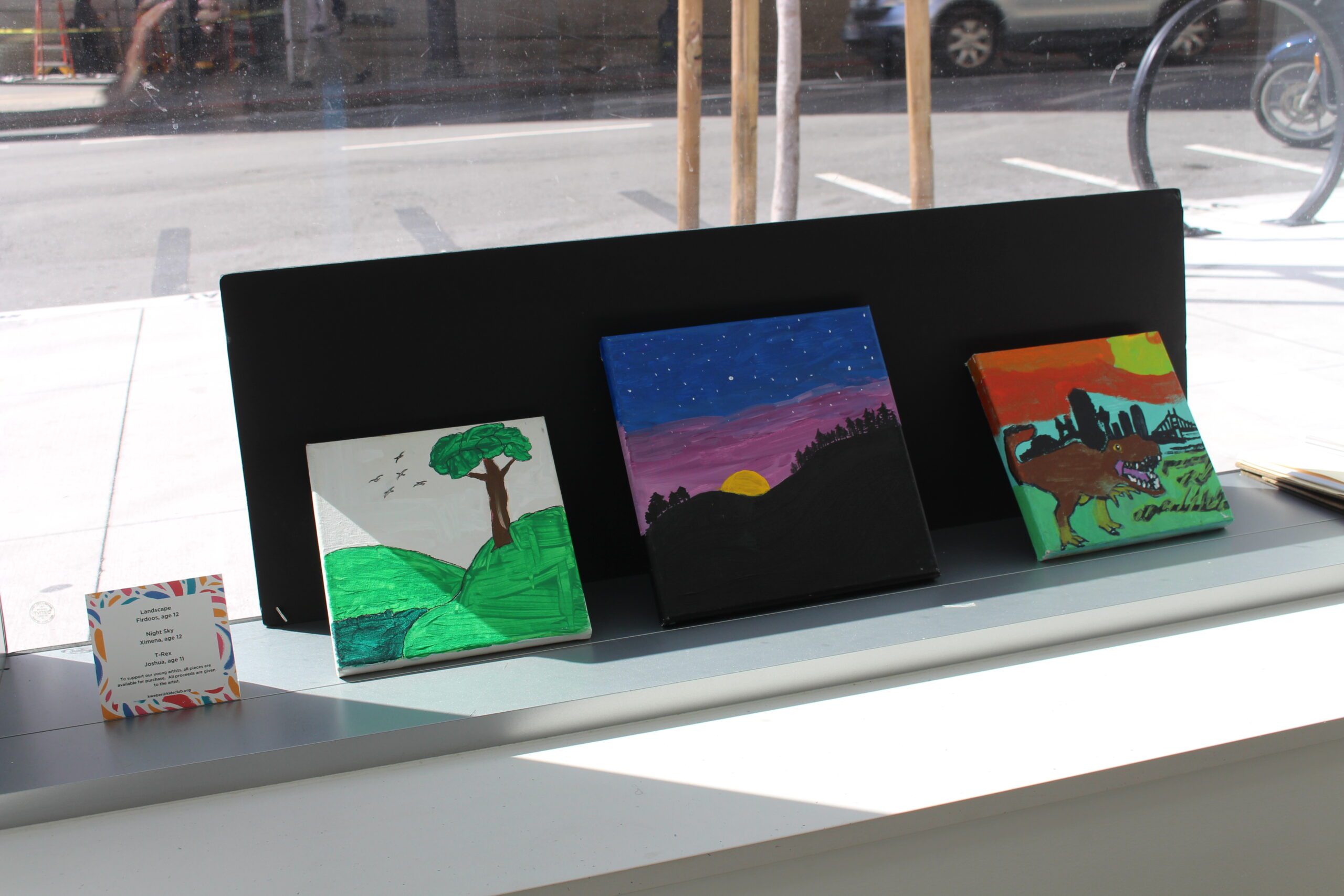 Three paintings on a shelf depicting outdoor scenes