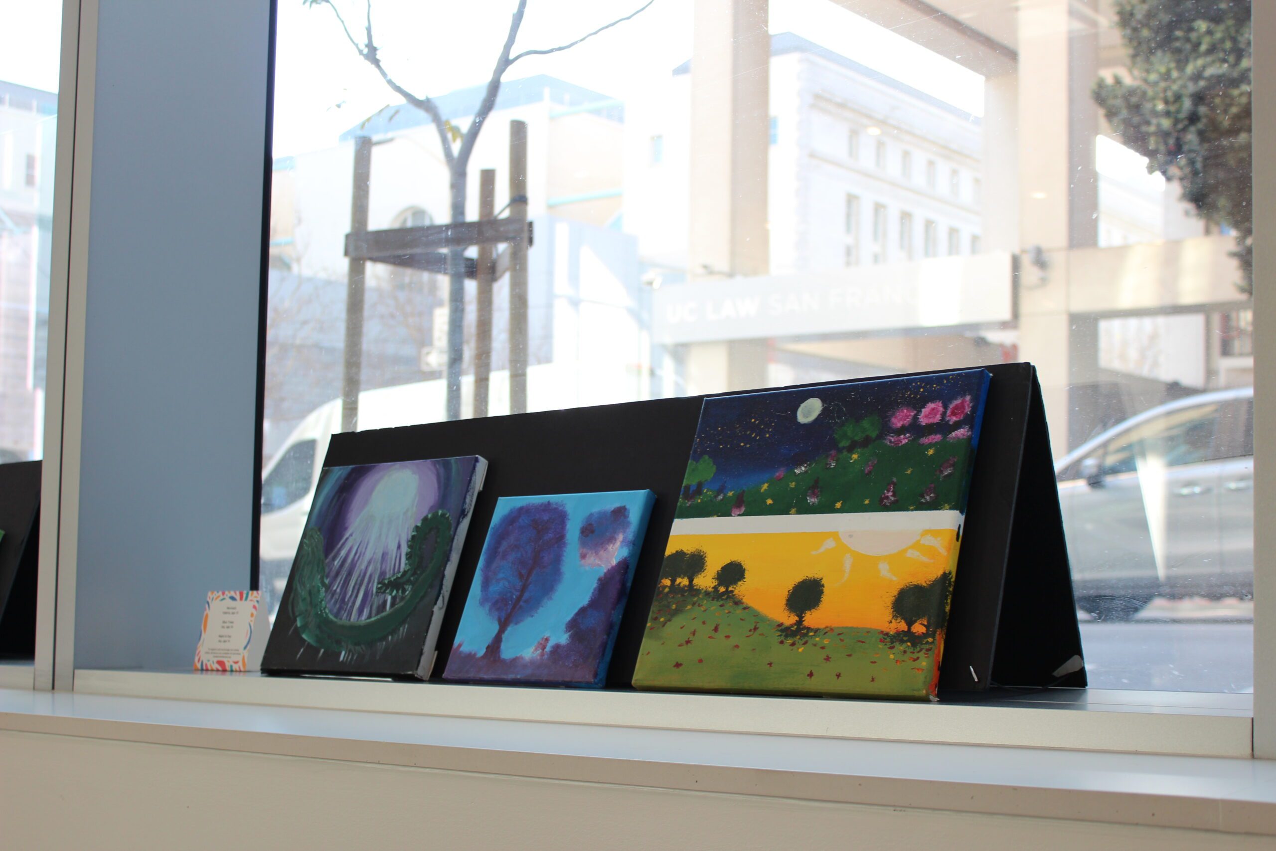 three paintings on a shelf depicting outdoor scenes