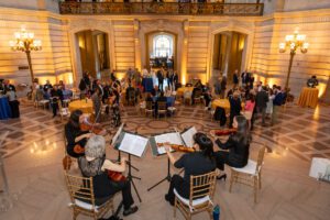 A string quartet plays on the steps inside City Hall as partygoers enjoy food and conversation.