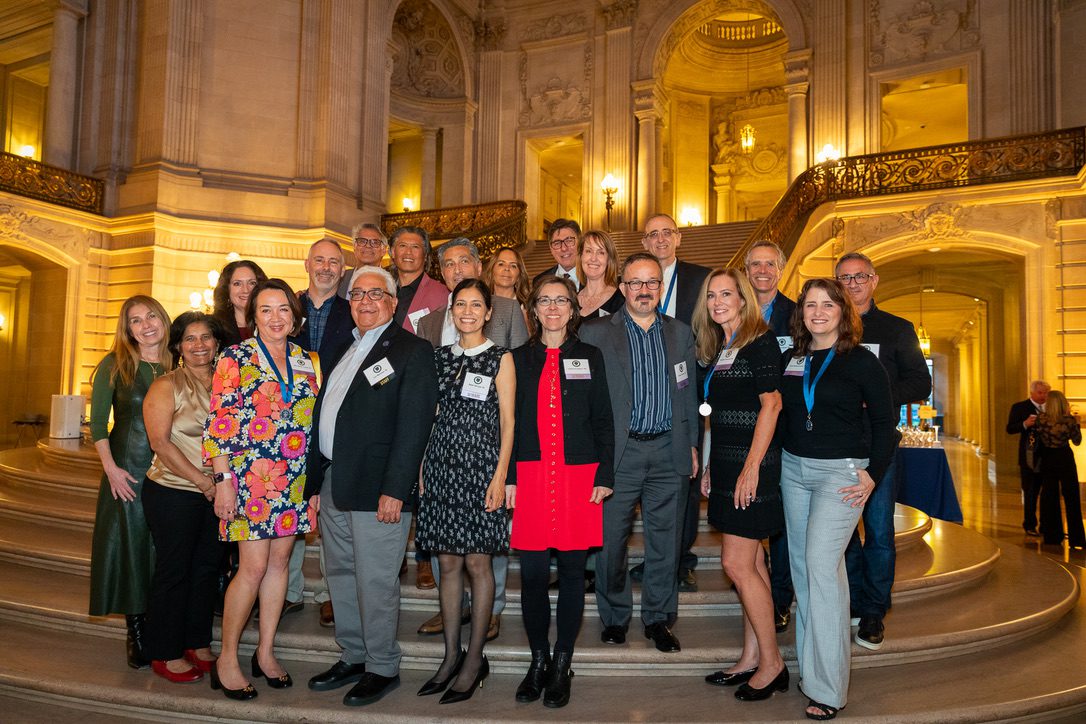 A group of UC LawSF alumni pose for a photo on the steps of the rotunda area inside San Francisco's City Hall.