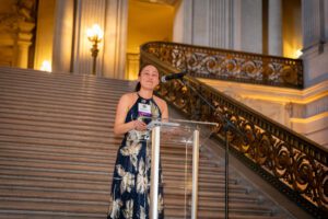 Kelly Matayhoshi speaks at a clear lectern in San Francisco's City Hall.