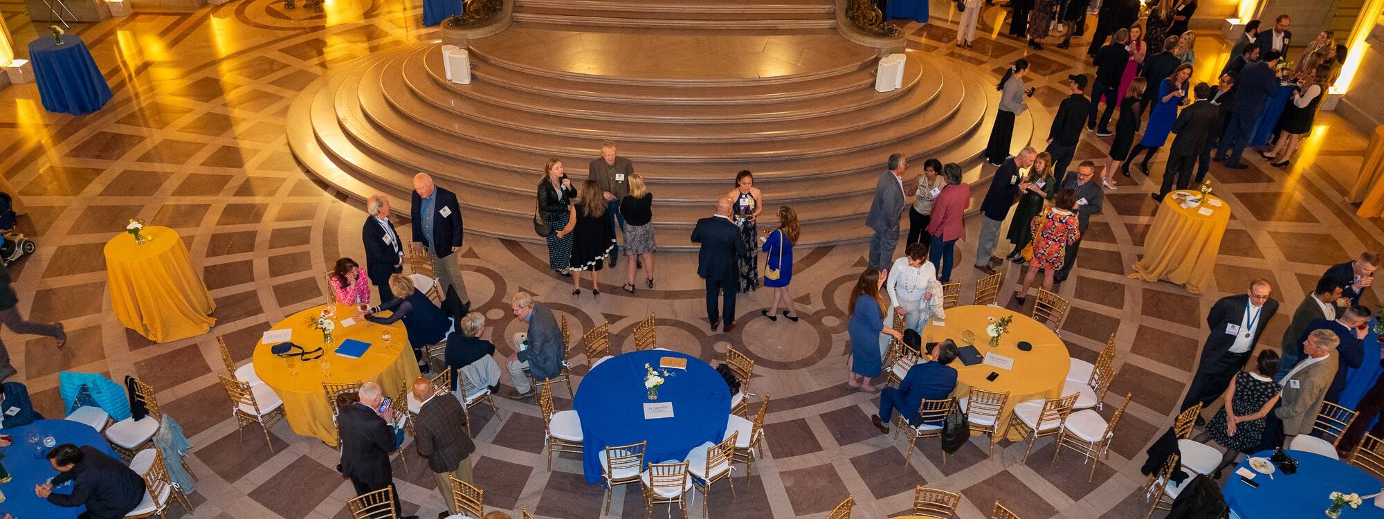 Partygoers enjoy the San Francisco City Hall rotunda room, set for a reception and decorated in blue and gold.
