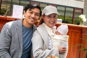 Two people pose with an infant while seated at a table.