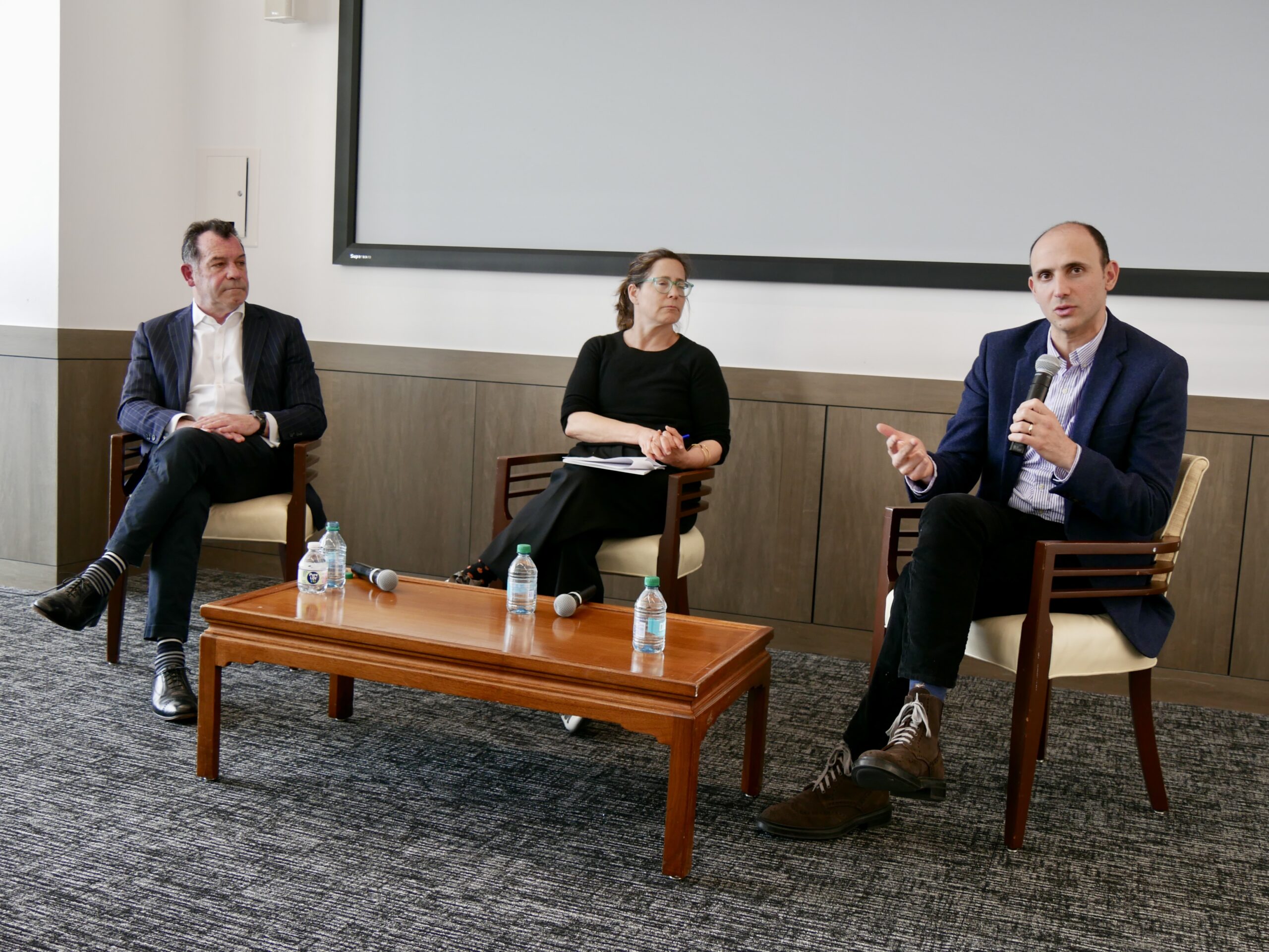 Three panelists are seated in chairs during a discussion.