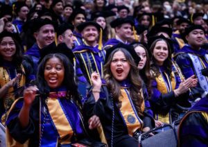 A crowd of happy graduates in caps and gowns seated it an auditorium